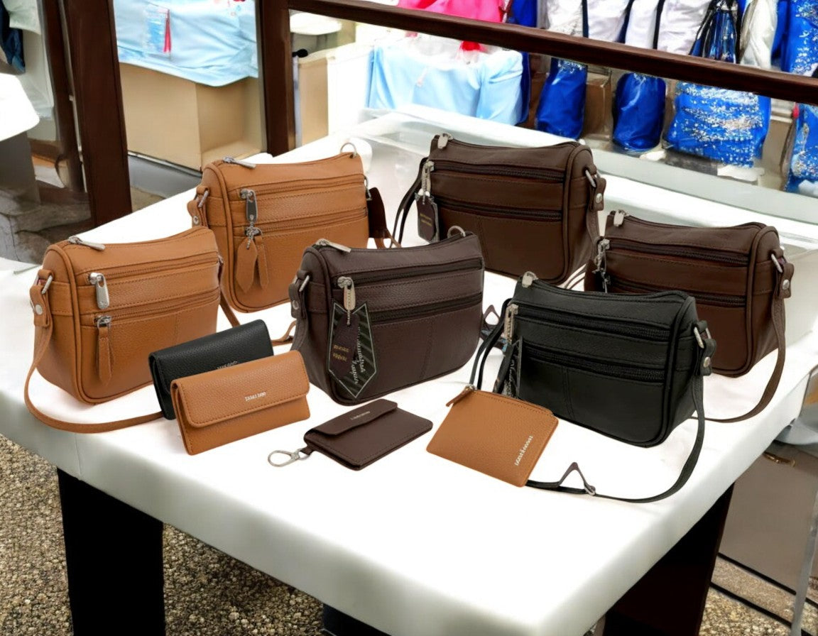 Collection of leather crossbody bags and wallets in tan, brown, and black displayed on white table in retail store setting