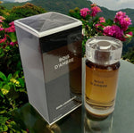 Karl Lagerfeld Bois d'Ambre perfume bottle and packaging on a reflective surface with flowers in the background
